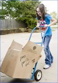 A girl pushing a dolly with boxes on it.