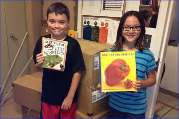 Two children holding books in front of a box.