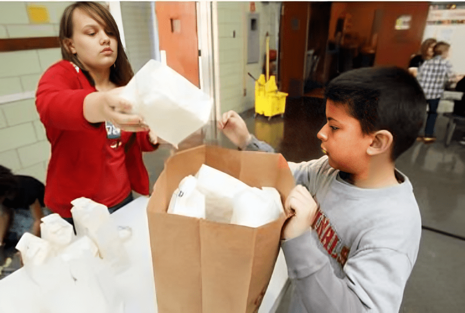 A boy and girl are putting paper in a bag.