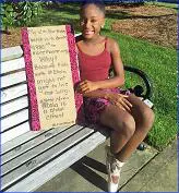 A young girl sitting on top of a bench holding up a sign.