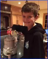 A boy is pouring something into a tea pot.