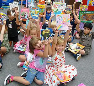 A group of children sitting on the ground holding books.