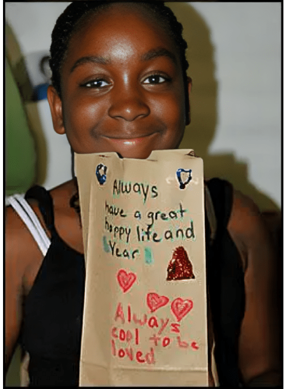 A young girl holding up a paper bag with writing on it.